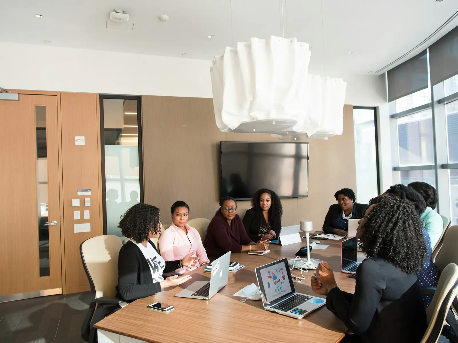 Diverse team of women meeting around a conference table with laptops in a bright office