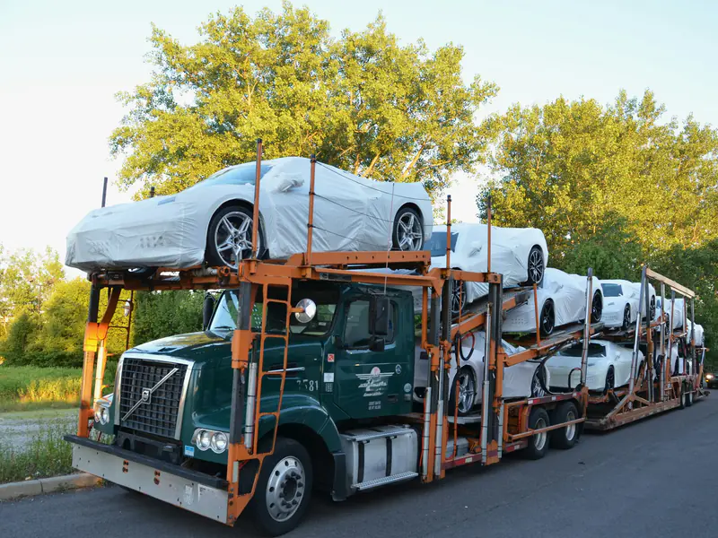 Car carrier truck loaded with new cars in white protective covers, parked at the roadside