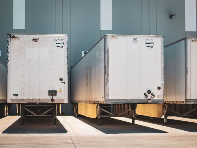 Three white dry-van trailers backed into numbered loading dock doors at a large distribution warehouse