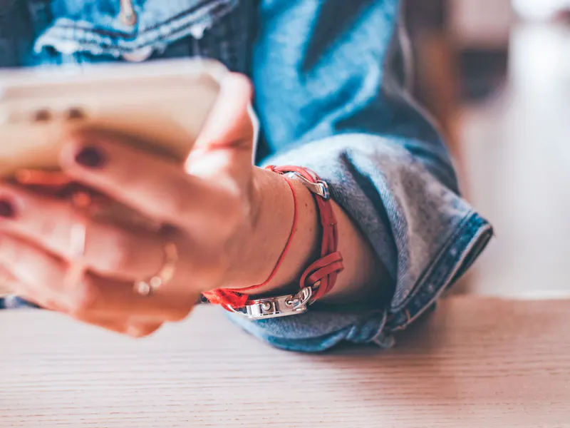 Close-up of hands with a ring and bracelets holding a smartphone at a light wooden table