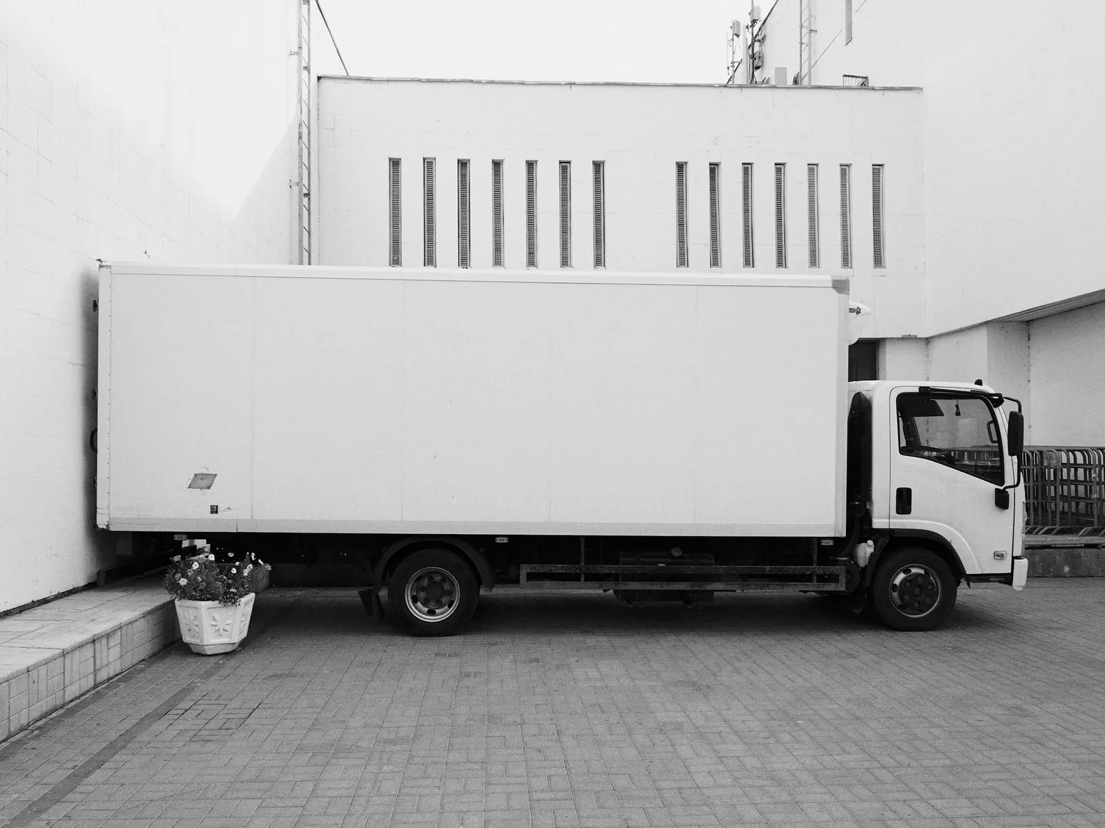 White box truck parked beside a white building on a paved yard