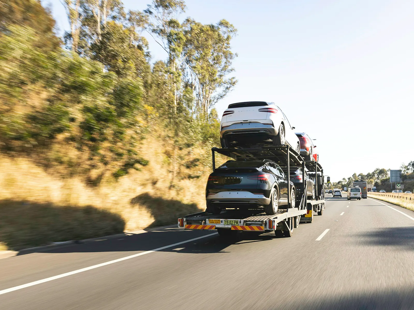 Car hauler loaded with cars on two decks driving along a highway, seen from behind with motion blur
