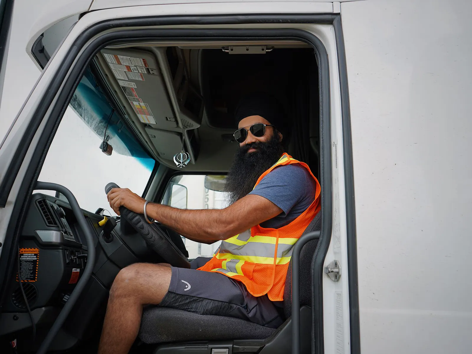 Truck driver in sunglasses and a hi-vis vest sitting behind the wheel of his cab, seen through the open door