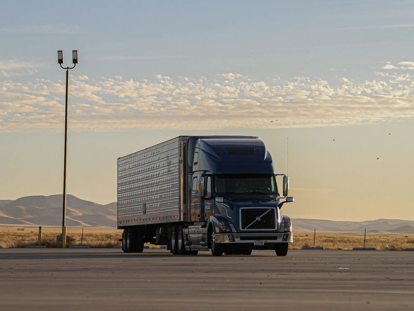 Black semi truck with a 53-foot dry van trailer parked on an open lot, with hills and an evening sky behind