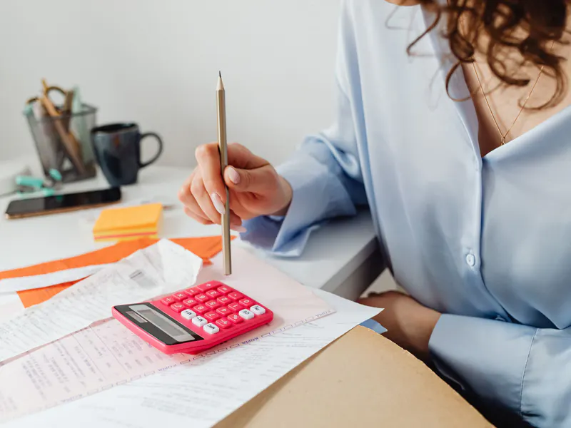 Woman at a white desk working through bills and receipts with a pencil and a pink calculator