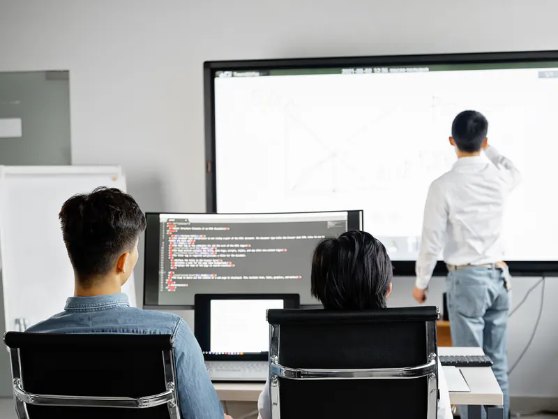 Trainer at a large screen walking staff through software while two employees follow along on their computers