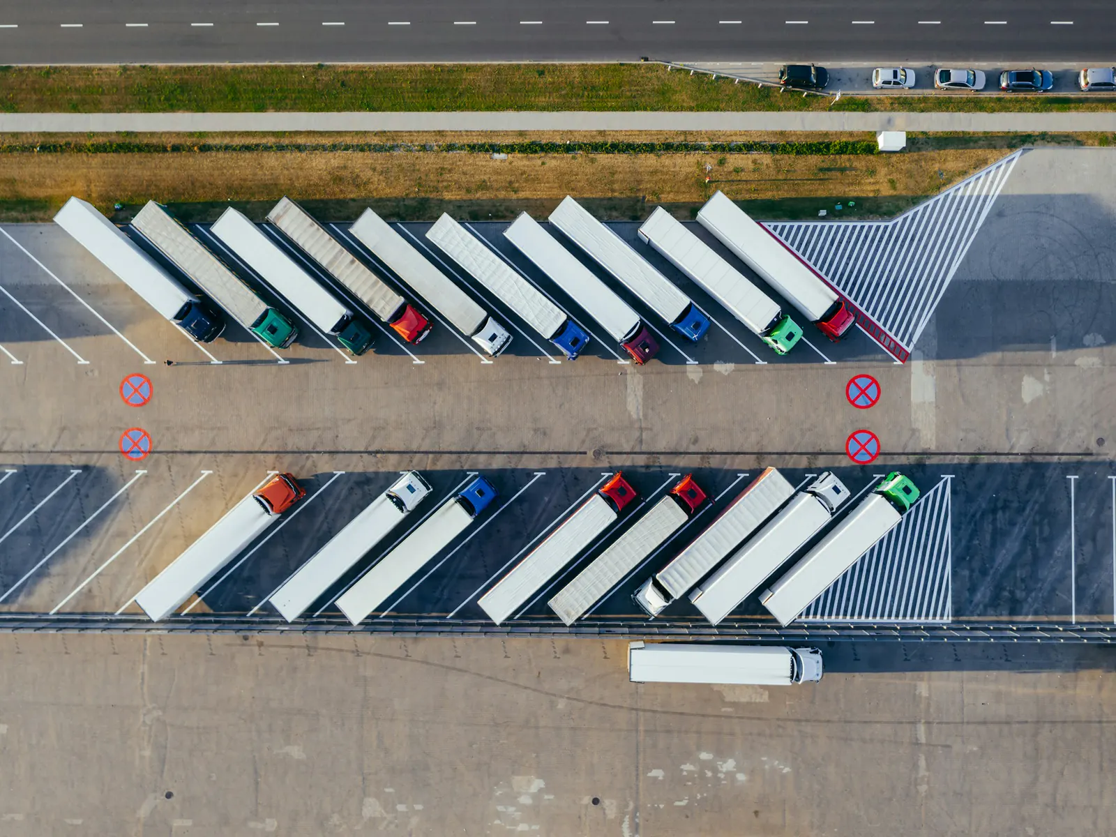Aerial view of two rows of semi trucks with white trailers parked at an angle in a truck lot