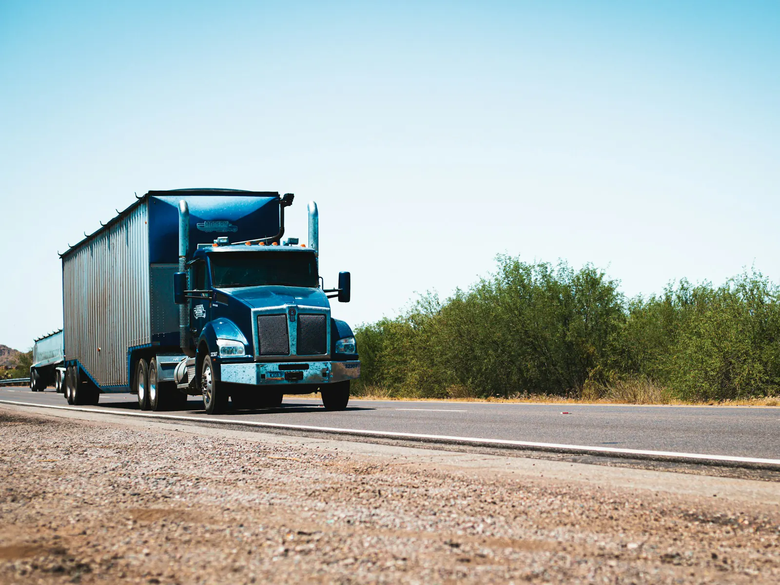 Shiny blue semi truck pulling a trailer along a desert road, shot low from the roadside