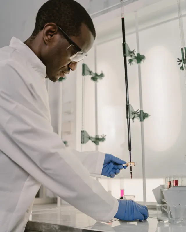 Scientist in a white lab coat, safety glasses and blue gloves working at a laboratory bench