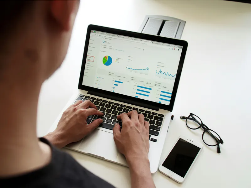 Over-the-shoulder view of a person typing on a laptop showing a website analytics dashboard on a white desk