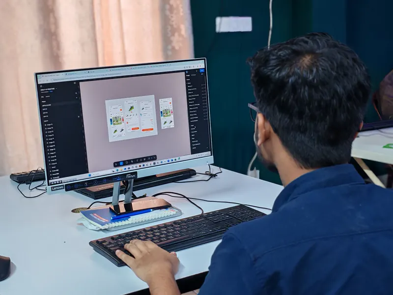 Designer seen from behind working on app and web screen layouts in a design tool on a desktop monitor